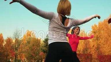年轻女子一起在<strong>秋季</strong>公园训练瑜伽锻炼教练。 苗条的女人练习户外<strong>健身</strong>运动